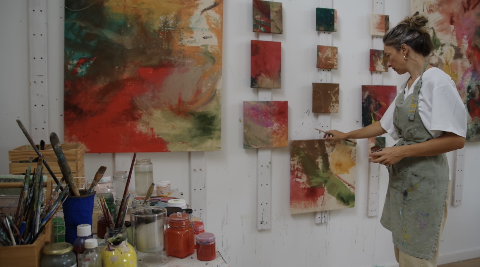 Nicky Myny in the studio working on small canvases with paint supplies nearby