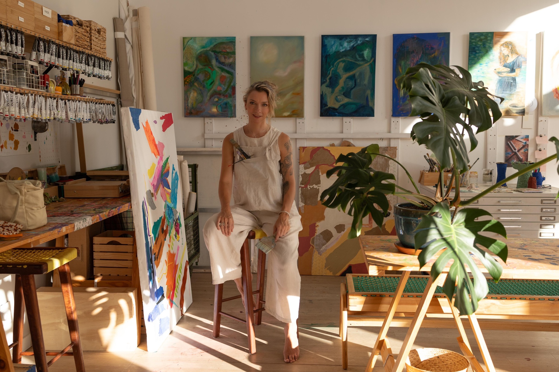 Nicky Myny seated on a stool in the studio surrounded by paintings
