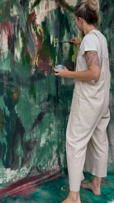 Nicky Myny painting into a large green canvas in her studio